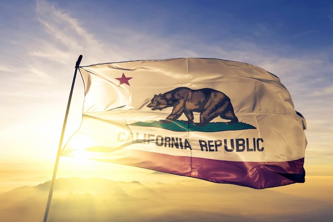 California state flag (Bear Flag) waving at sunrise above a mountain horizon