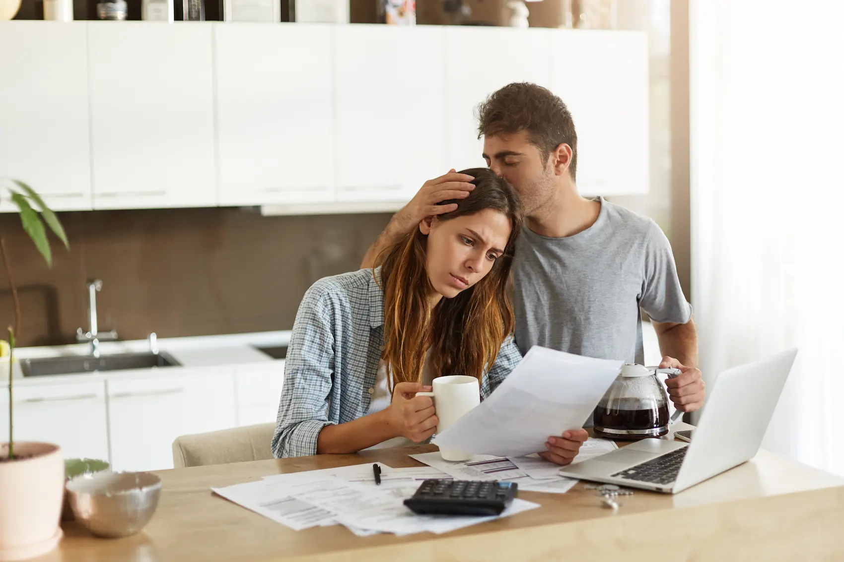 A couple sitting at a table looking concerned, representing the question of whether one spouse can file bankruptcy without the other.
