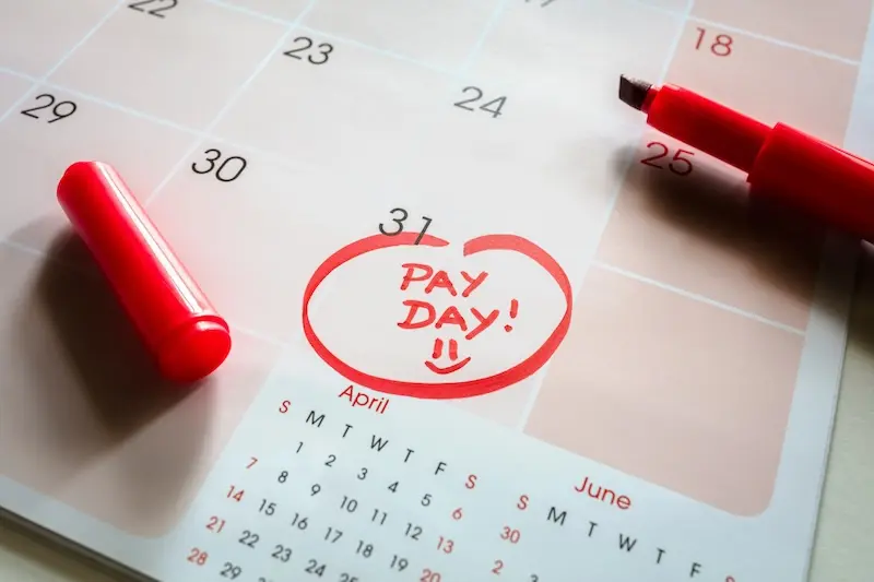 Photo of a calendar with the words 'Pay Day!' written in red ink, with a red pen lying on top of the calendar.